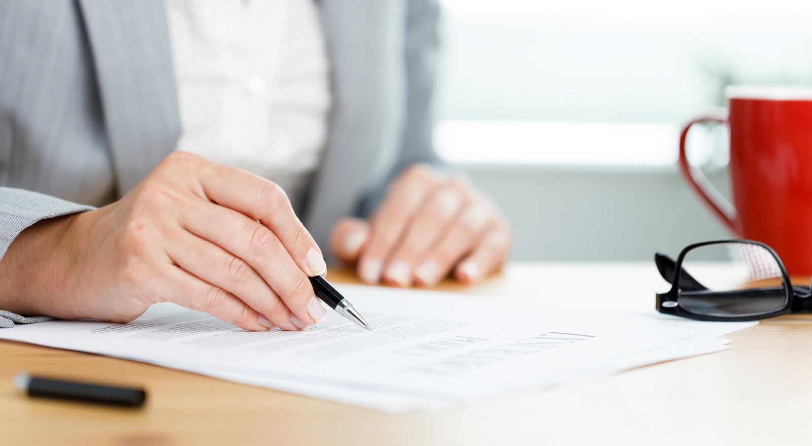 A woman closely reviewing and filling out an insurance policy document at her office desk