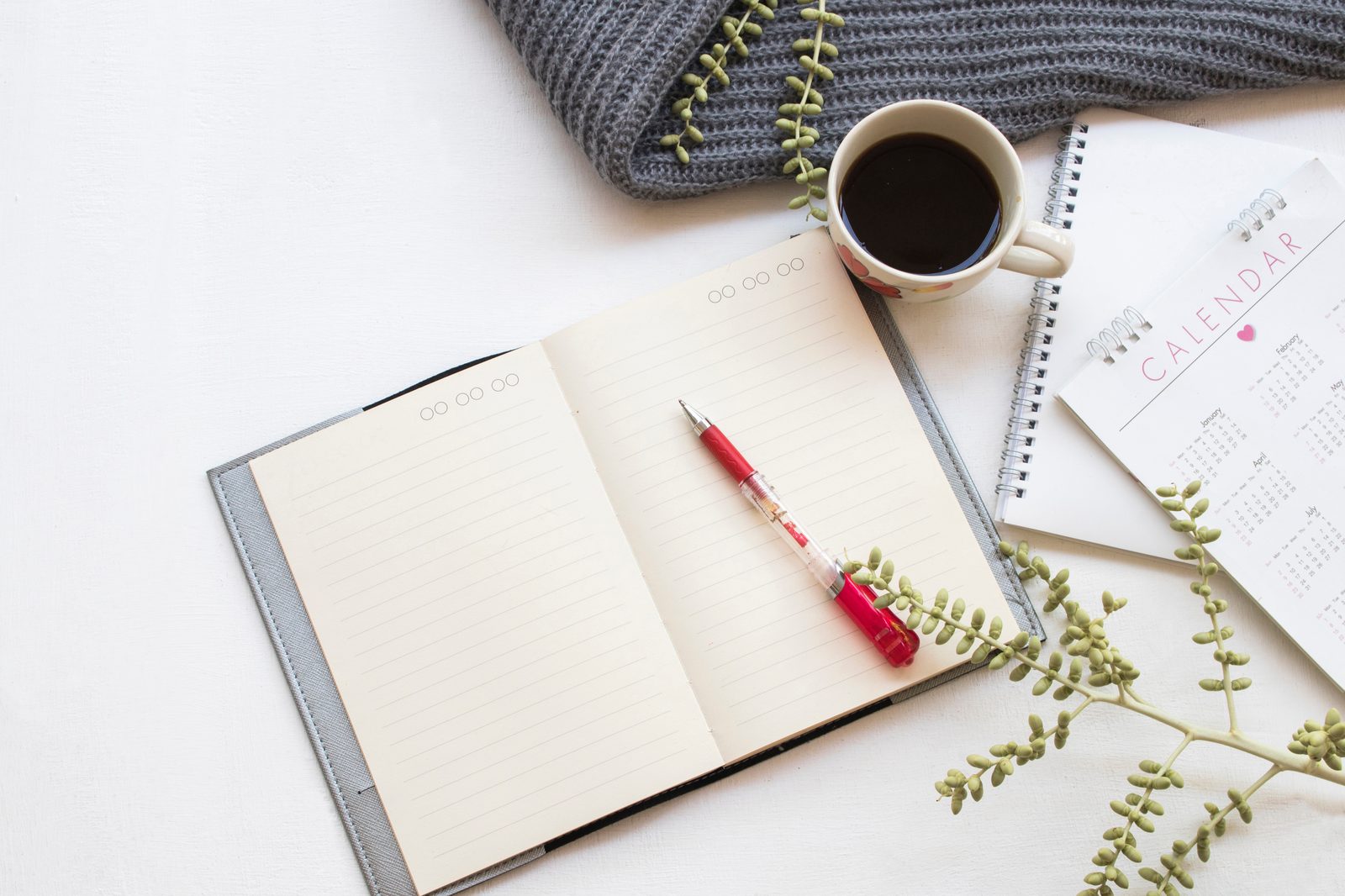 A planner and calendar open on a desk next to a cup of coffee