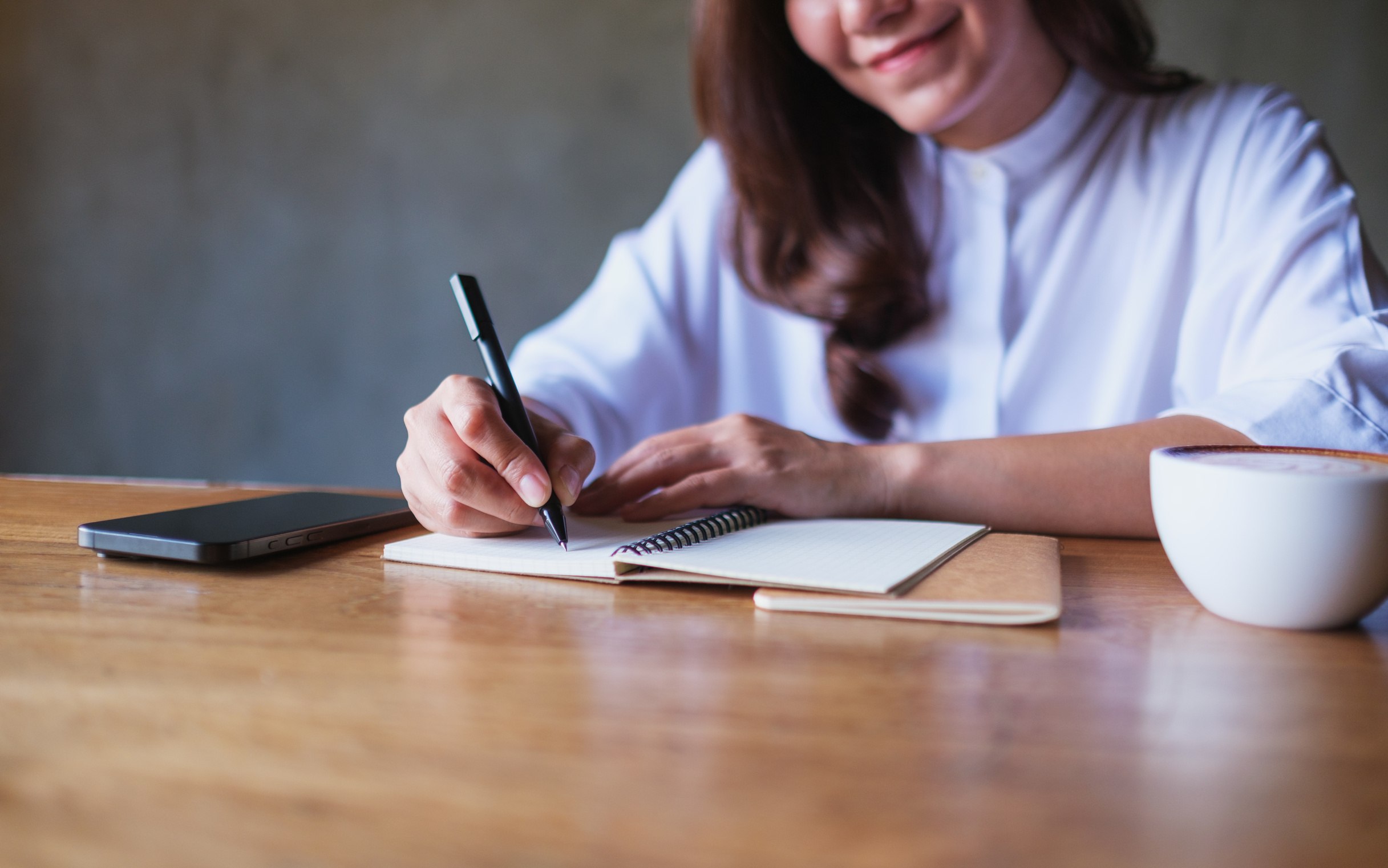 A program staff member writing budget notes by hand next to a cup of coffee