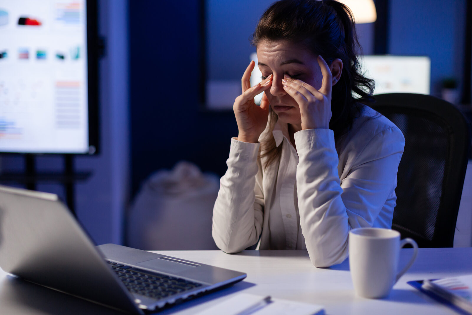 A program manager sitting at a desk, visibly tired, rubbing her eyes